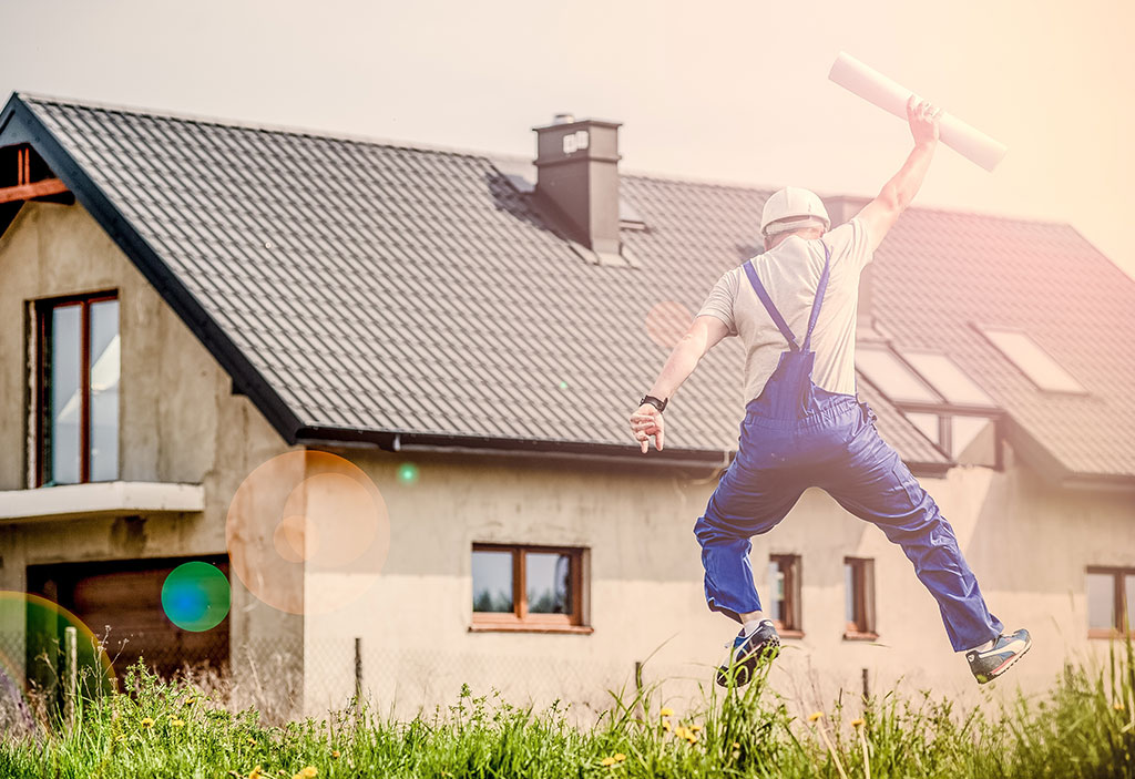 Man in overalls jumping into the air holding building plans